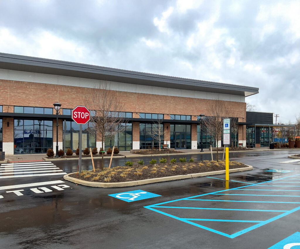 A row of vacant storefronts with a brick facade, a stop sign, and a blue-painted accessible parking space in the foreground.
