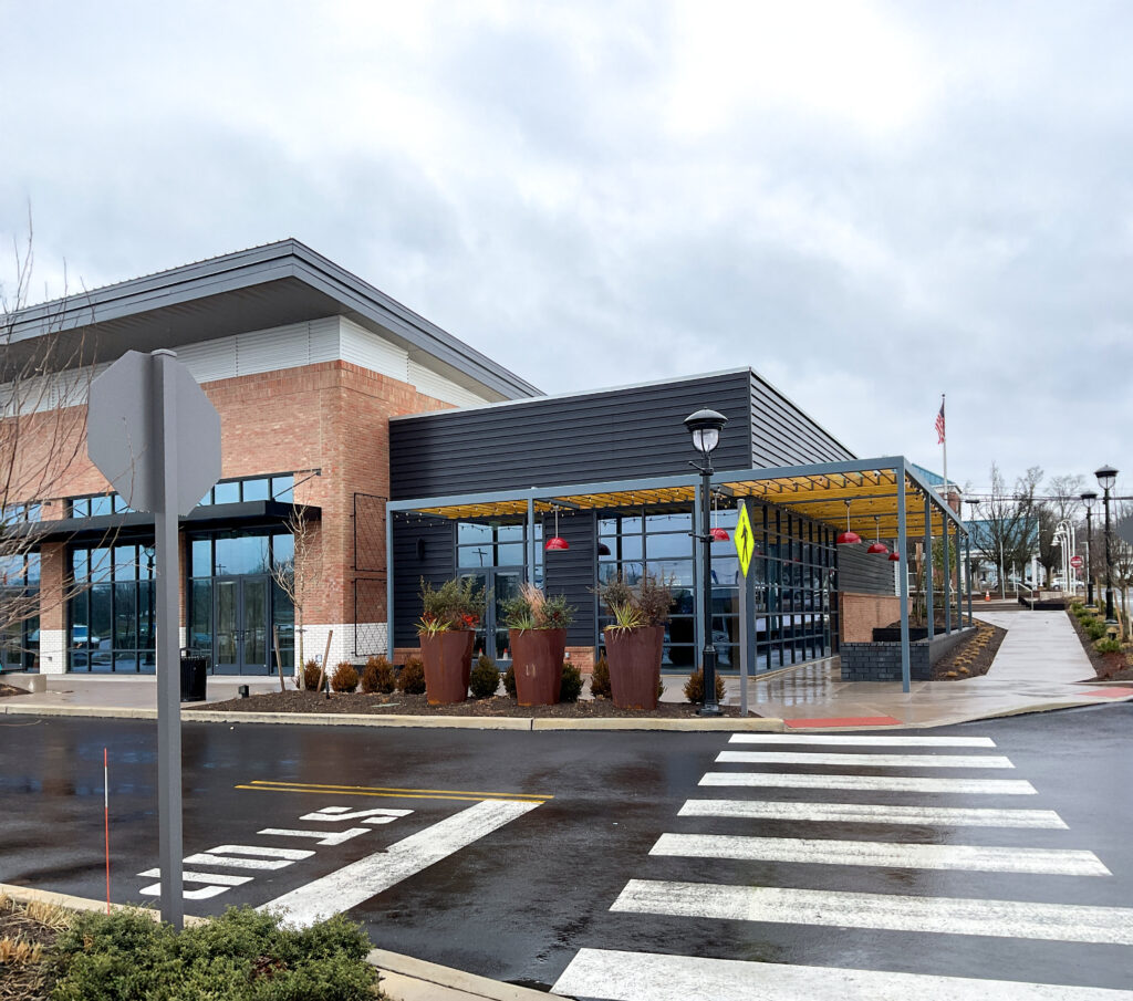 Modern commercial building with a brick and black siding facade, featuring a covered outdoor patio with planters and a pedestrian crosswalk in the foreground.