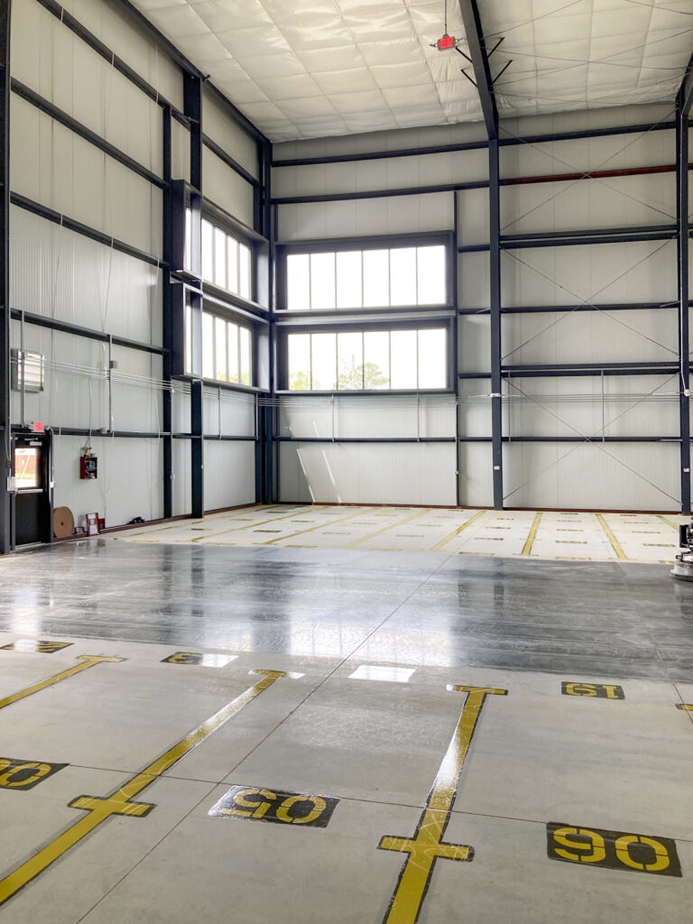 Empty warehouse interior with tall windows and numbered parking spaces painted on the concrete floor.