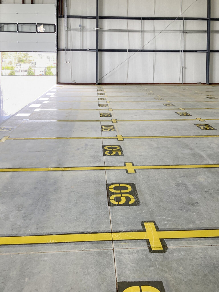 An empty warehouse floor with rows of parking spaces marked by yellow lines and sequential numbers.