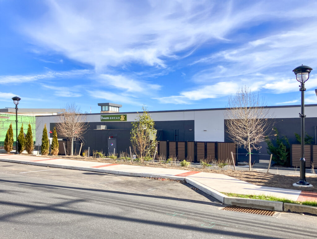 The exterior of a Panera Bread restaurant with a parking lot and sidewalk in the foreground.