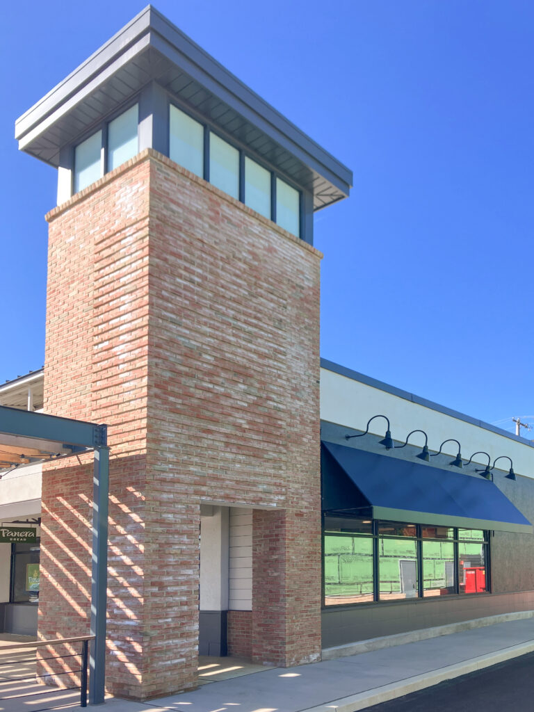 A brick building tower with a dark blue awning over the windows and a Panera Bread sign visible on the left.