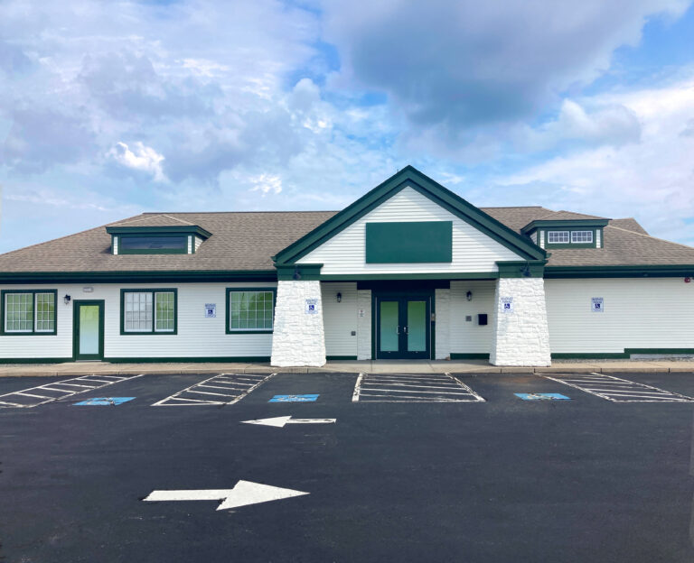 Exterior of a single-story commercial building with white siding, a green gabled roof, and designated handicap parking spaces in the foreground.