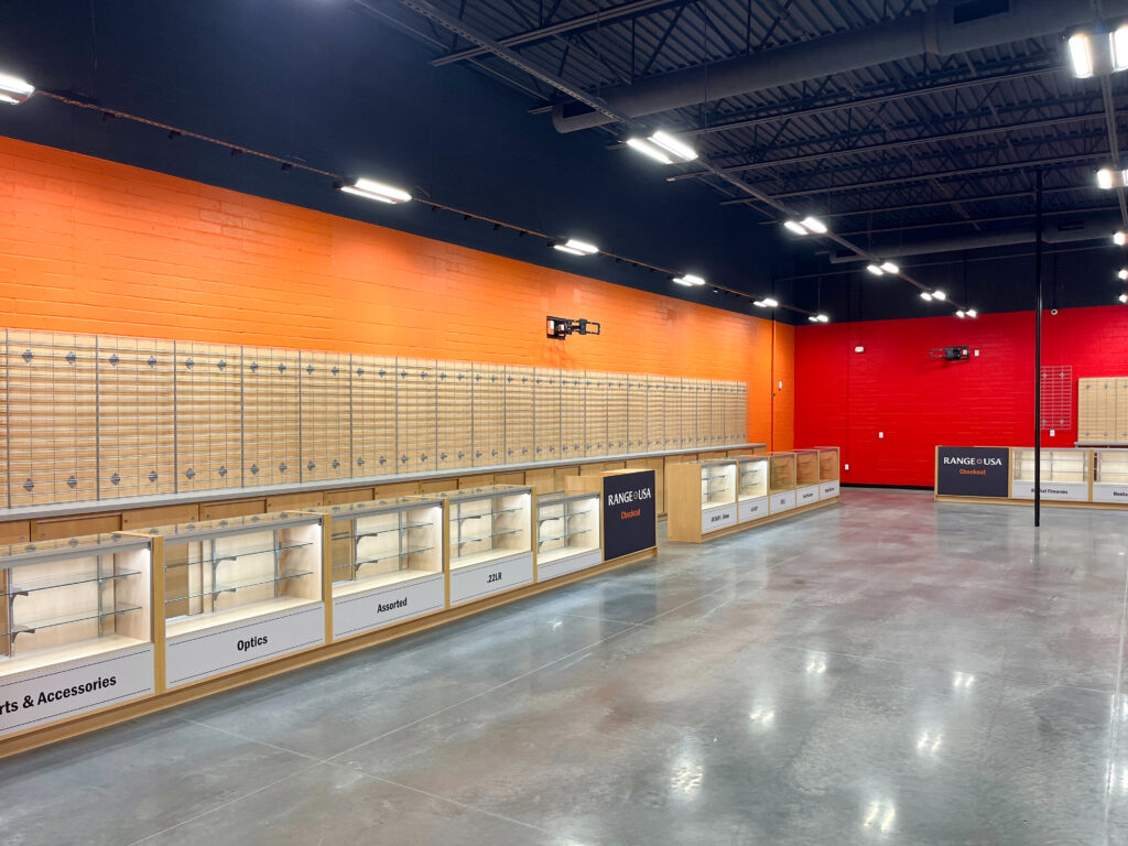 Interior of a retail store with empty glass display cases along orange and red walls, featuring a Range USA checkout counter.