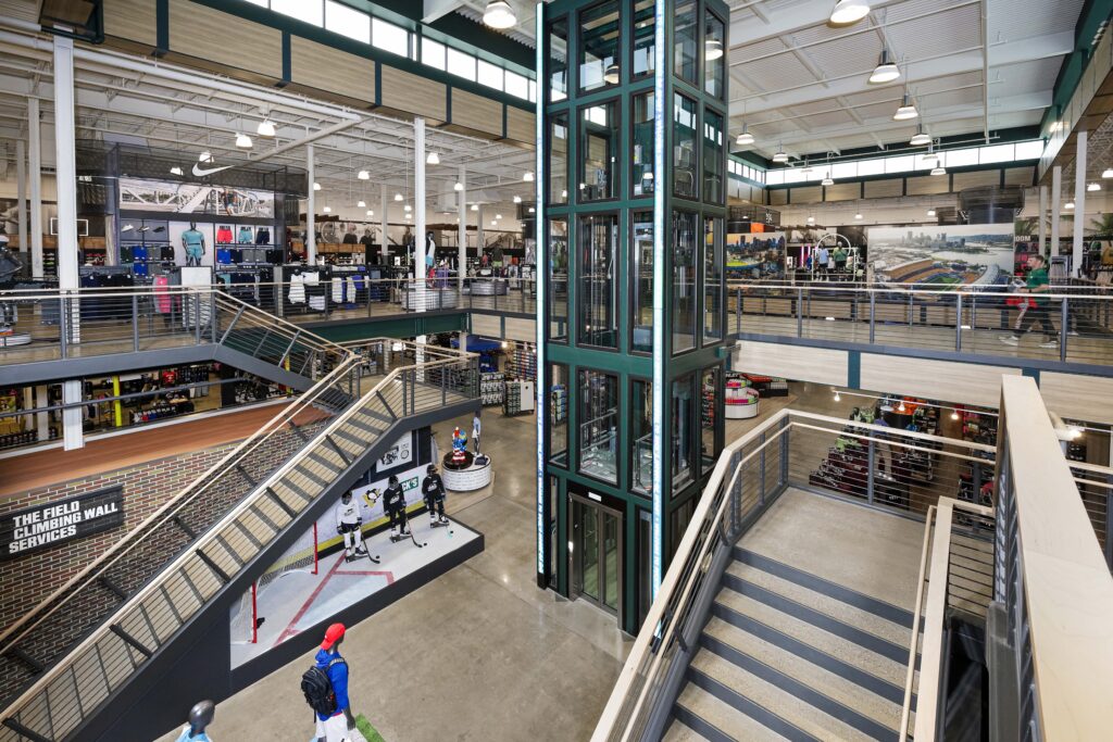 Interior view of a multi-level sports store featuring a central glass elevator, staircases, and displays for hockey gear and apparel.