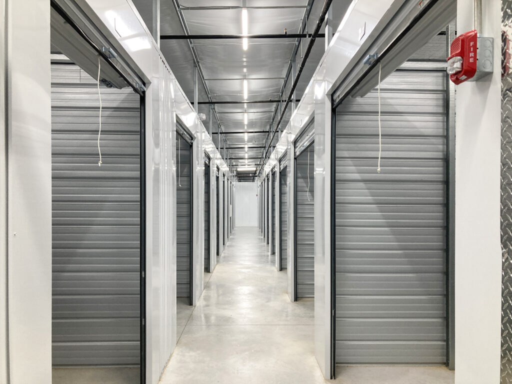 A hallway lined with rows of closed metal storage units and a red fire alarm on the wall.