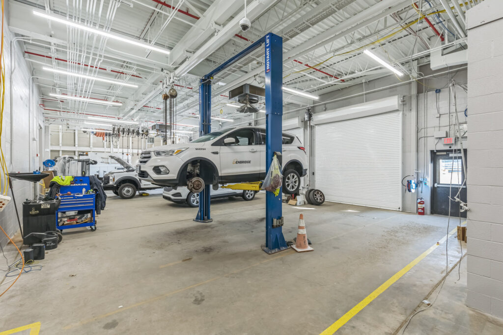 White SUV lifted on a hydraulic car lift in an auto repair shop.