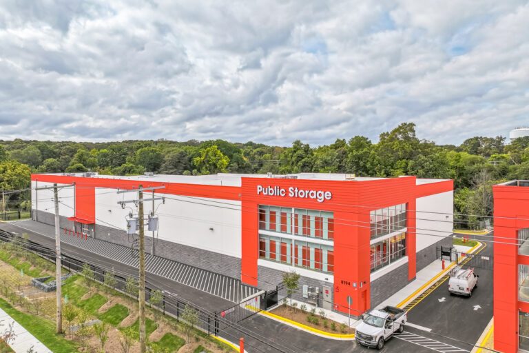 A Public Storage facility building with a red and white facade, surrounded by a parking lot with two trucks.