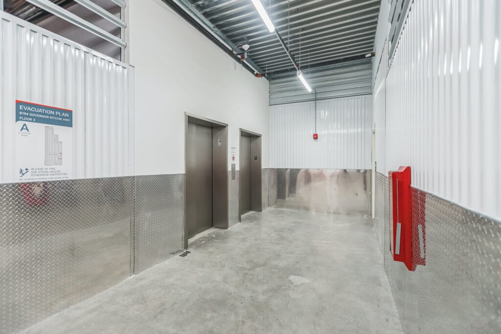Two silver elevators in a storage facility hallway with metal walls and a fire extinguisher.