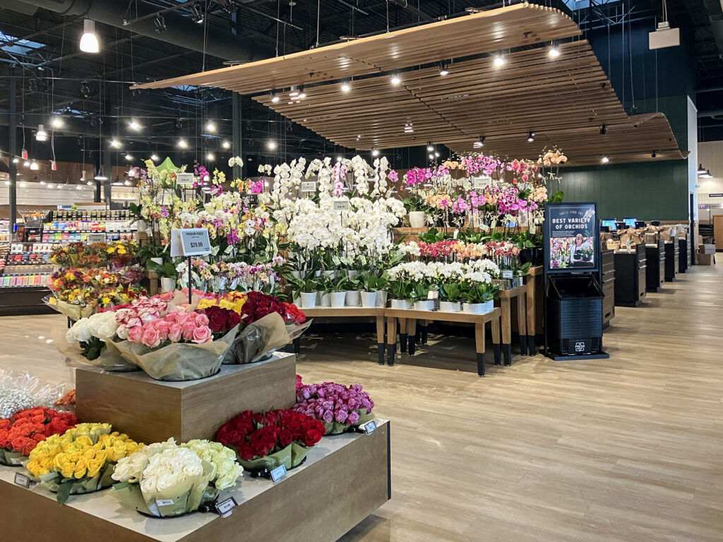 Floral department in a grocery store featuring tiered displays of various colored roses and a large selection of white and pink orchids.