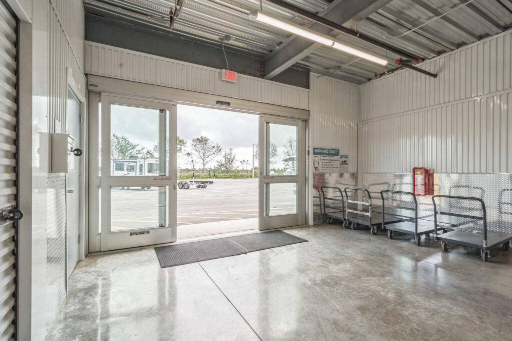 Open sliding glass doors in a storage facility, with flatbed moving carts parked inside near a wall.