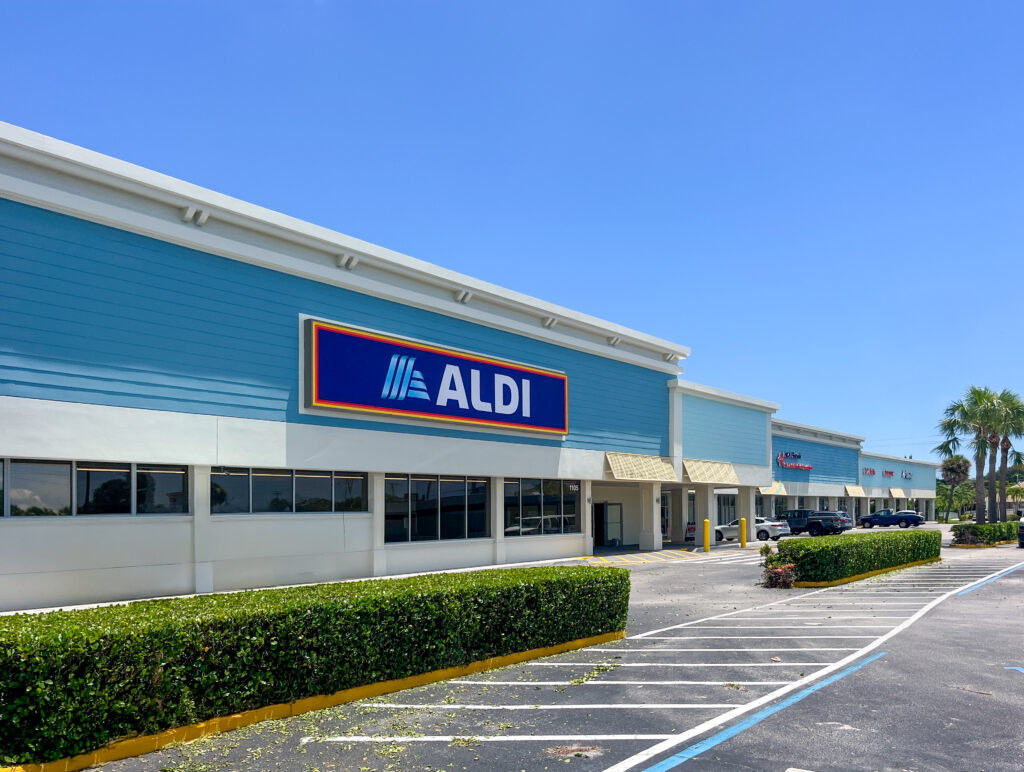 Exterior of an Aldi grocery store in a strip mall with a blue facade and parking lot.