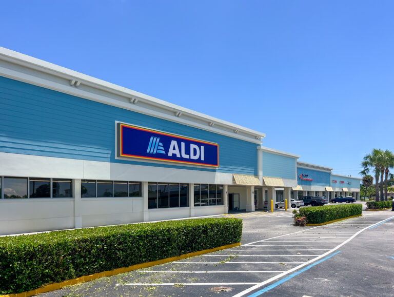 Exterior of an Aldi grocery store in a strip mall with a blue facade and parking lot.
