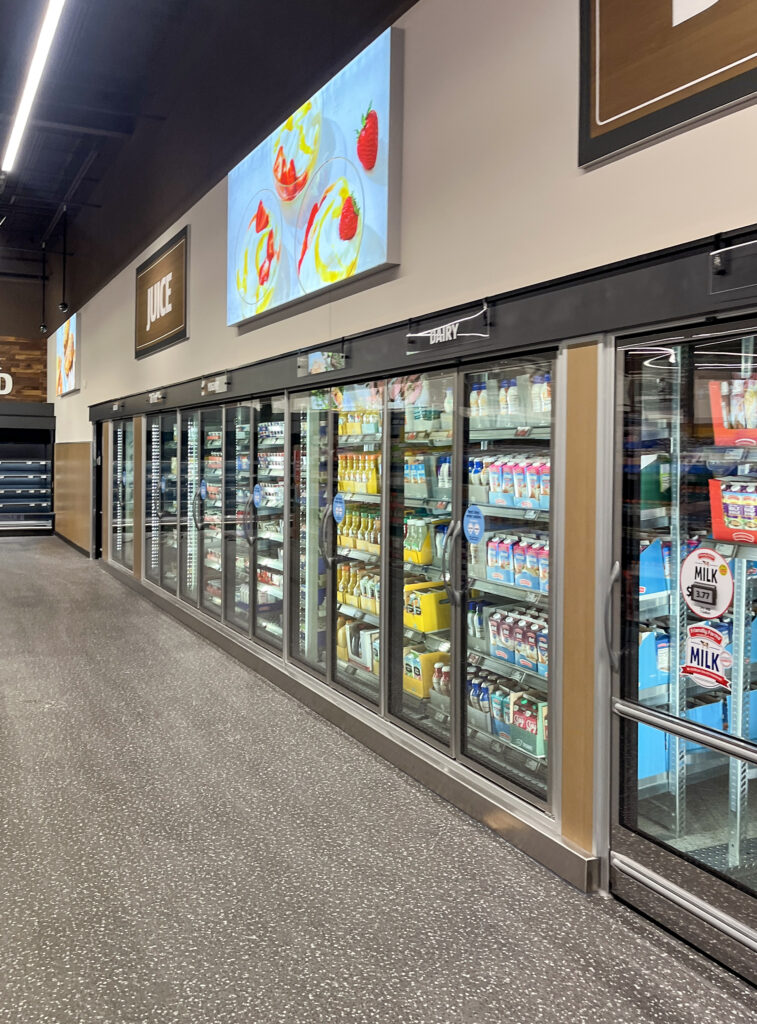 A grocery store refrigerated aisle featuring rows of glass-door coolers stocked with juice and dairy products.