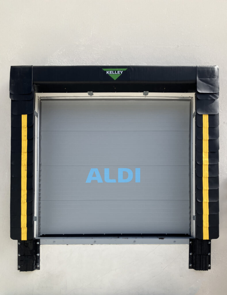 A closed loading dock door with an Aldi logo centered on the grey panels and a Kelley brand label at the top.