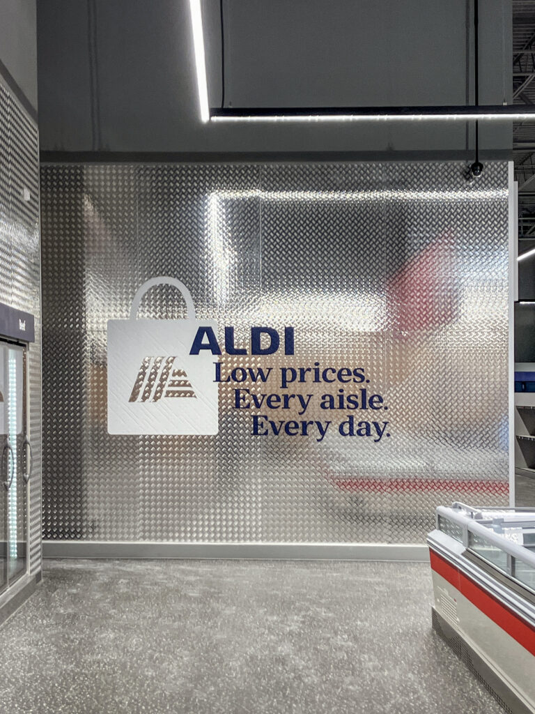 ALDI logo and slogan “Low prices. Every aisle. Every day.” displayed on a diamond plate metal wall.