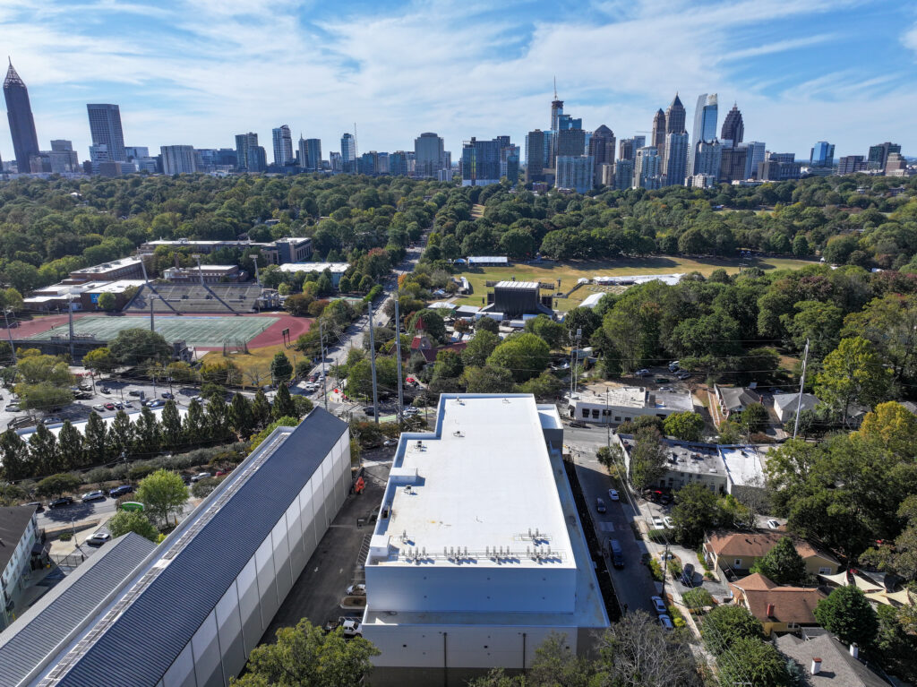 Aerial view of a city skyline rising above a large park, with industrial buildings in the foreground.