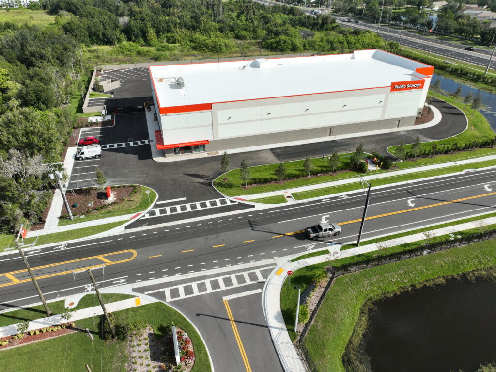 Aerial view of a Public Storage facility with a white roof, adjacent parking lot, and a nearby road intersection.