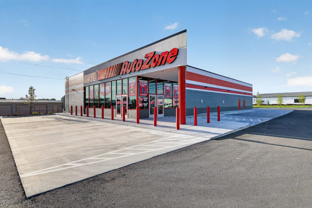 Exterior view of an AutoZone store with a large parking lot and red bollards in front of the building.