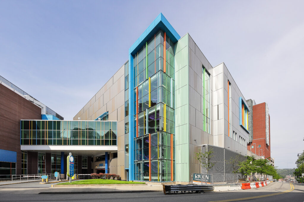 Modern multi-story building featuring a glass facade with colorful vertical accents and a covered driveway entrance.