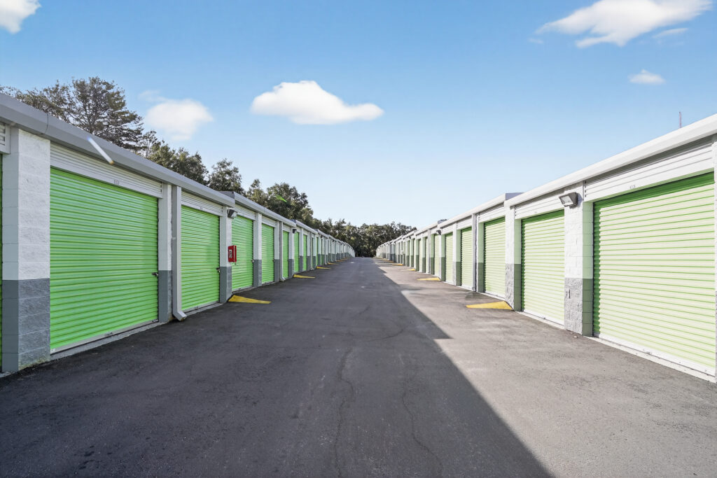 A row of self-storage units with lime green roll-up doors facing an asphalt driveway.