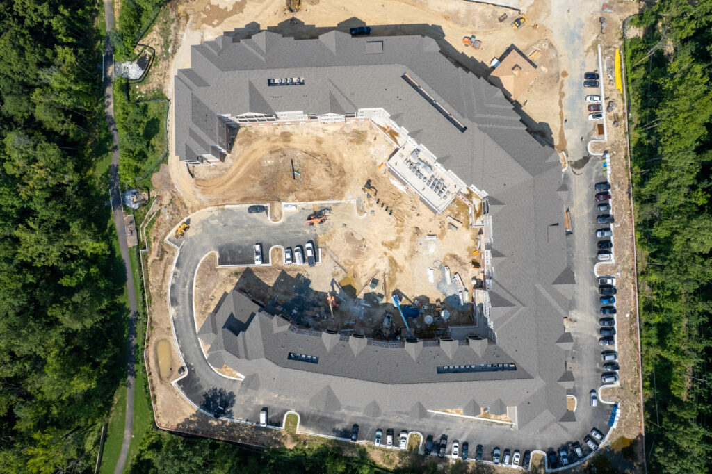 Aerial view of a U-shaped apartment building under construction, surrounded by trees and paved parking areas.