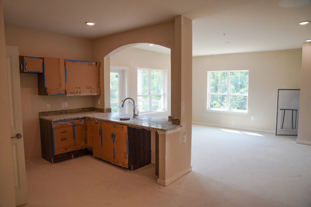 A kitchen under construction featuring an L-shaped granite countertop, a stainless steel sink, and cabinets covered in protective cardboard.