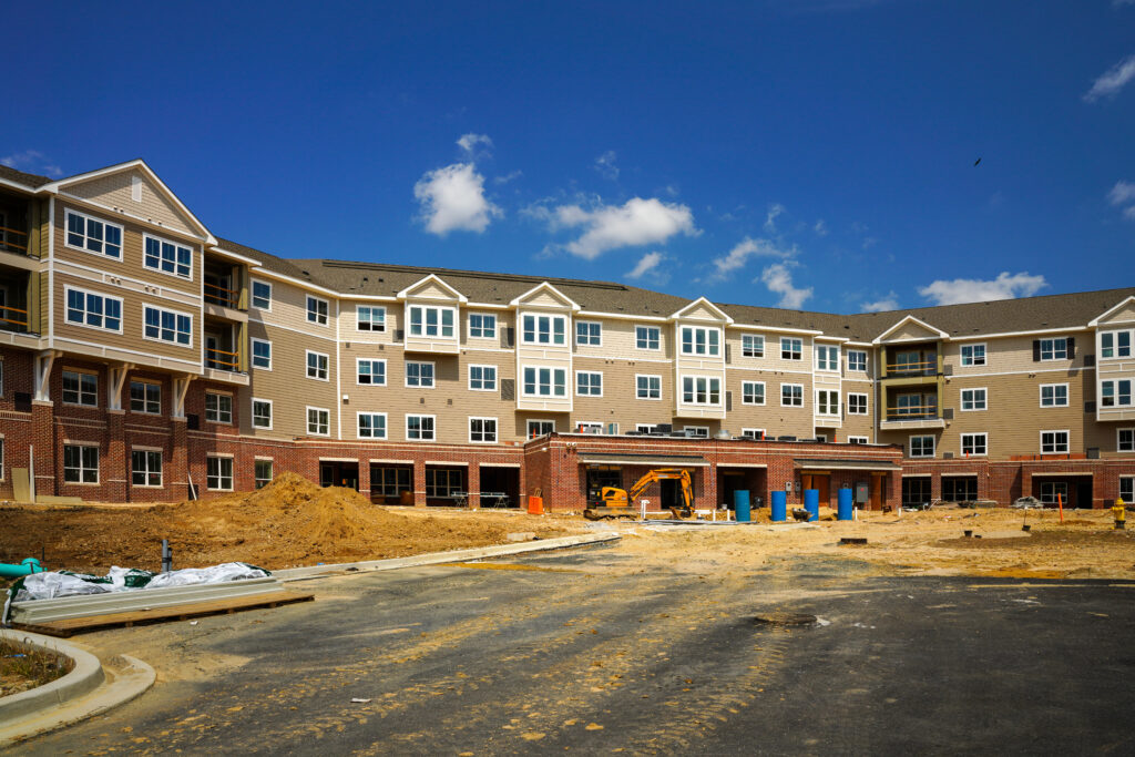 A multi-story apartment complex under construction with an unpaved lot in the foreground.