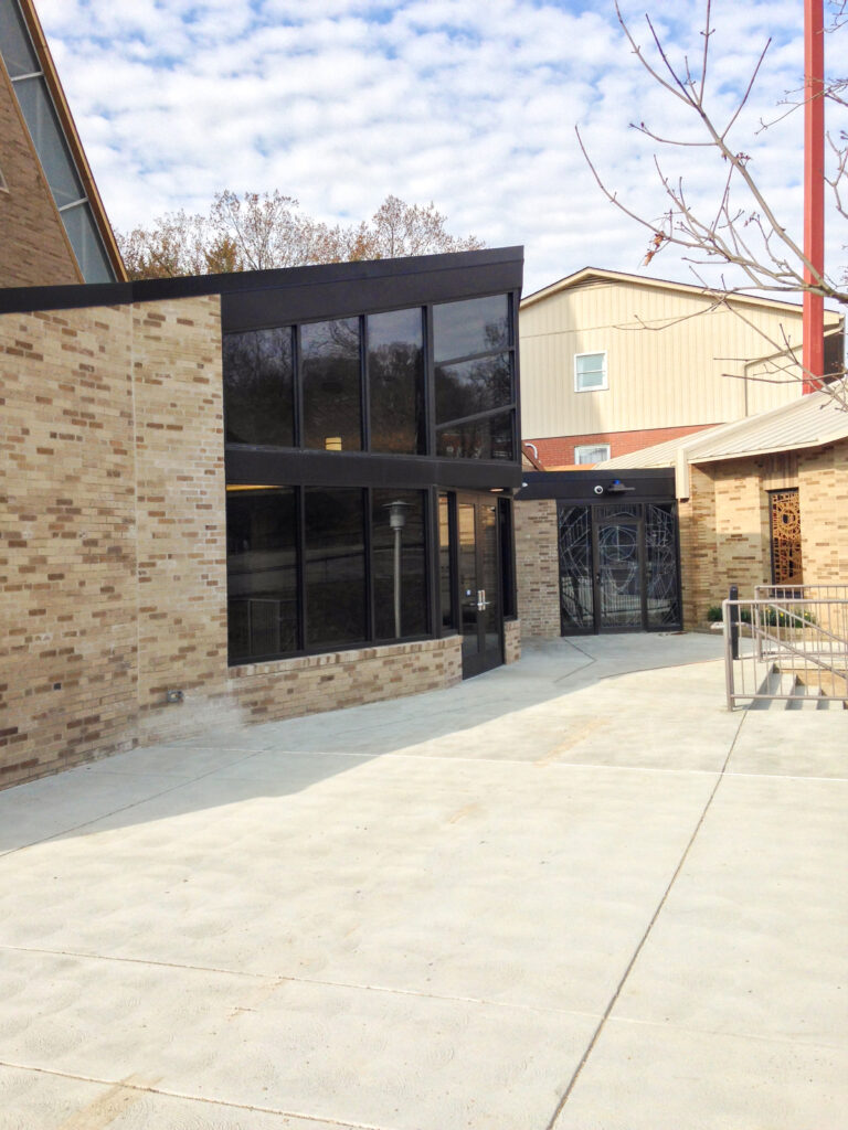 Entrance to a brick building with floor-to-ceiling windows and a glass door featuring a metal geometric design.