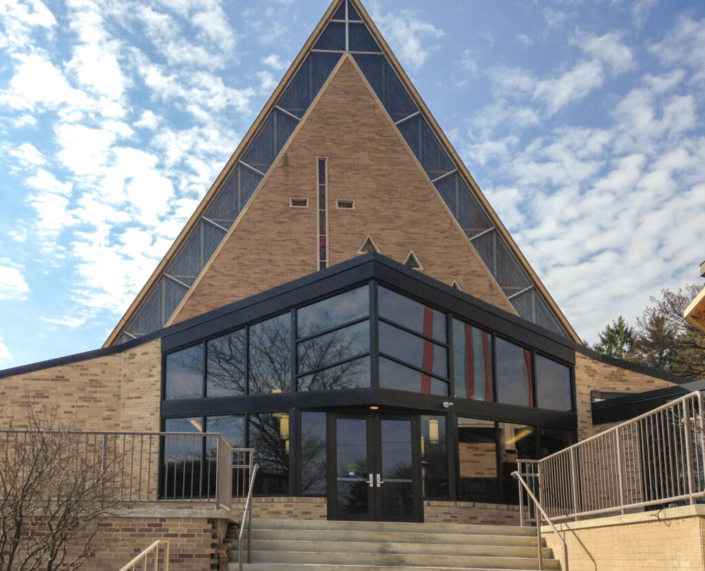 The triangular facade and glass-fronted entrance of a brick church building.