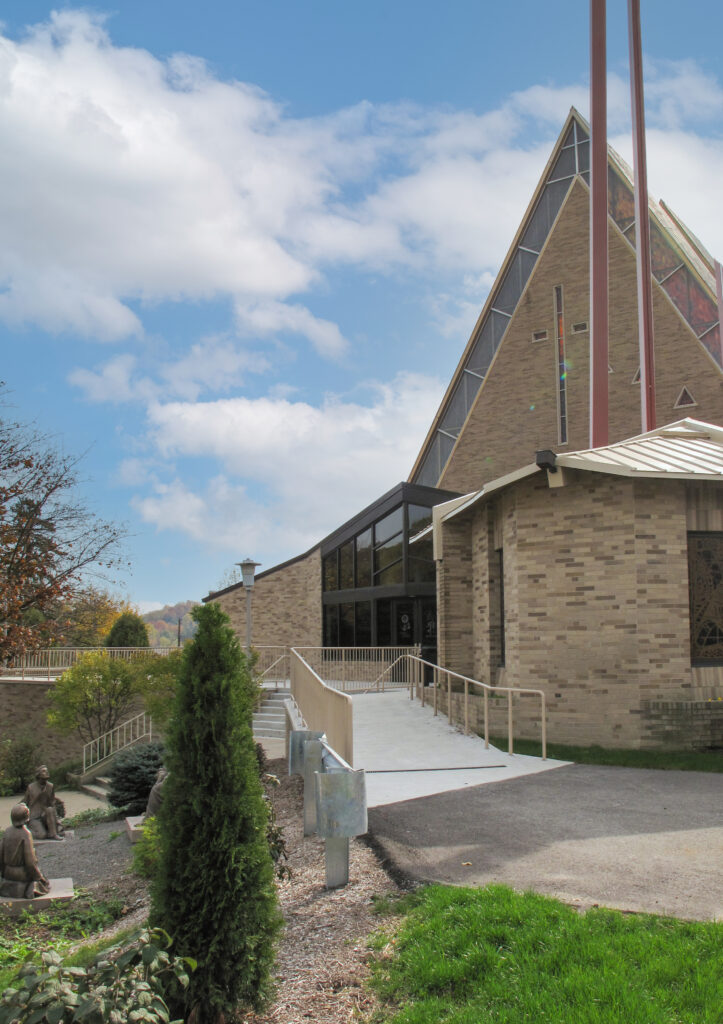 A brick church with a steeply pitched roof and a wheelchair ramp leading to the entrance.