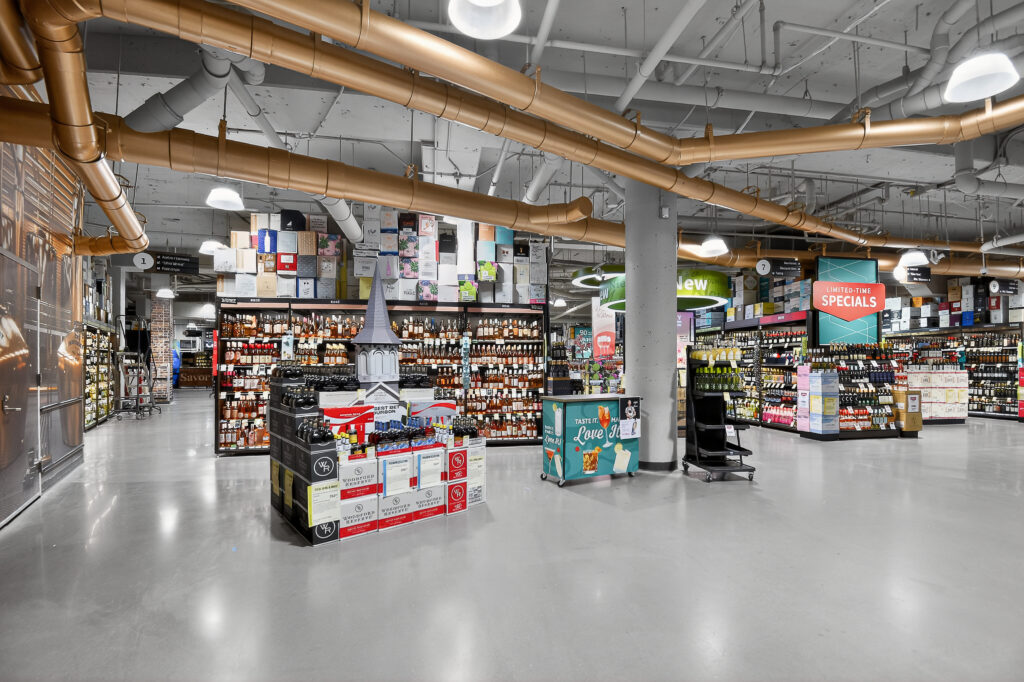 Interior of a liquor store with wide aisles, floor-to-ceiling shelves of bottled spirits, and a central display of Woodford Reserve bourbon cases.