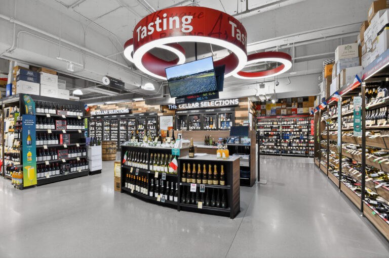 Interior of a wine shop with shelves of bottled wine and a central tasting station featuring a red circular sign and a digital display.