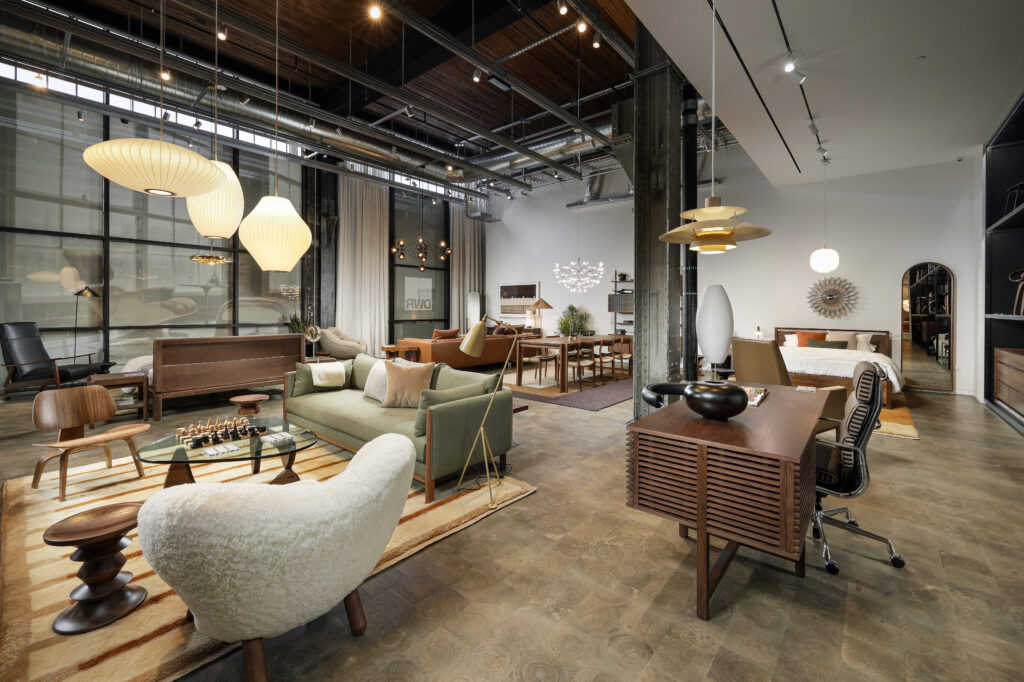 A wide view of a modern furniture showroom featuring living room, dining, and bedroom setups with various sofas, tables, and lighting fixtures.
