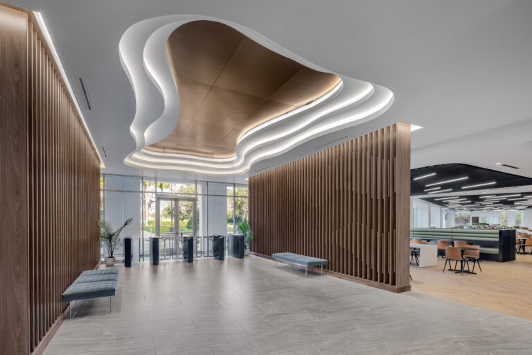 Modern office lobby with a curved, tiered ceiling feature, wood-slat walls, and glass entry turnstiles.