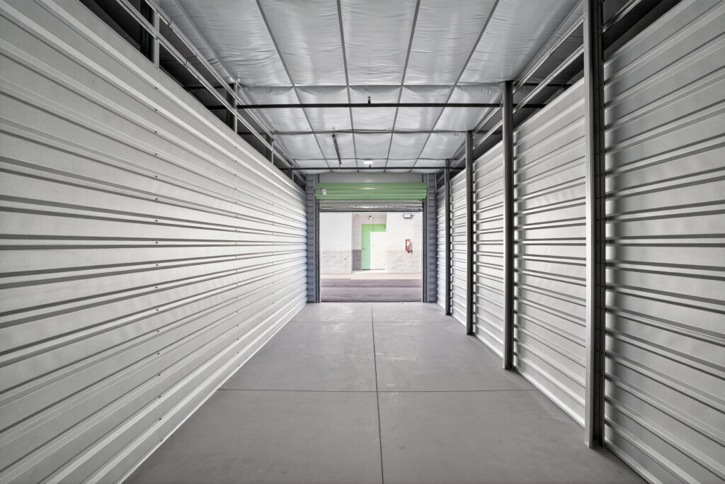 Empty storage unit with white corrugated metal walls, looking out toward an open doorway.