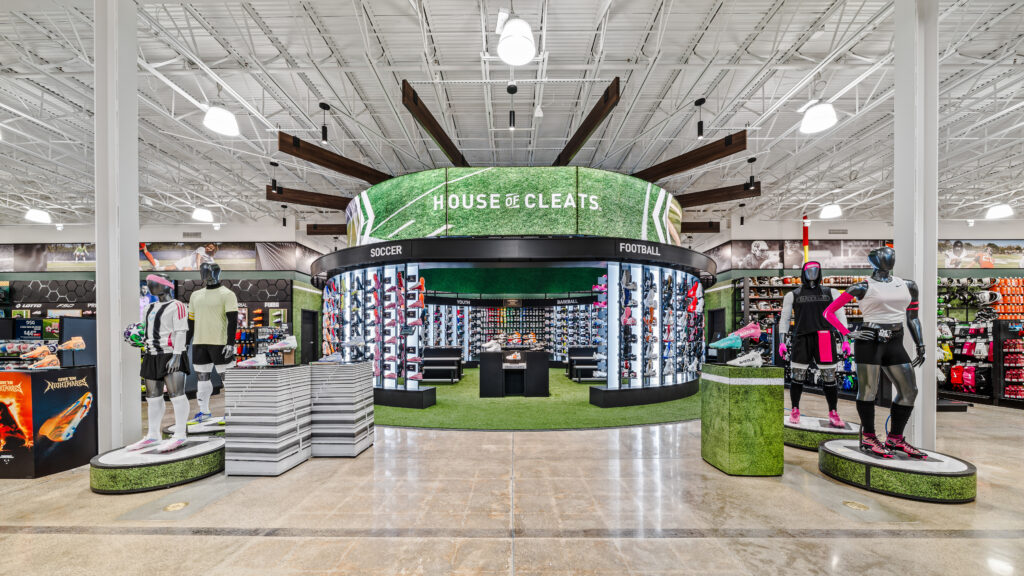 A circular “House of Cleats” display in a retail store, featuring rows of soccer and football shoes on illuminated shelves.