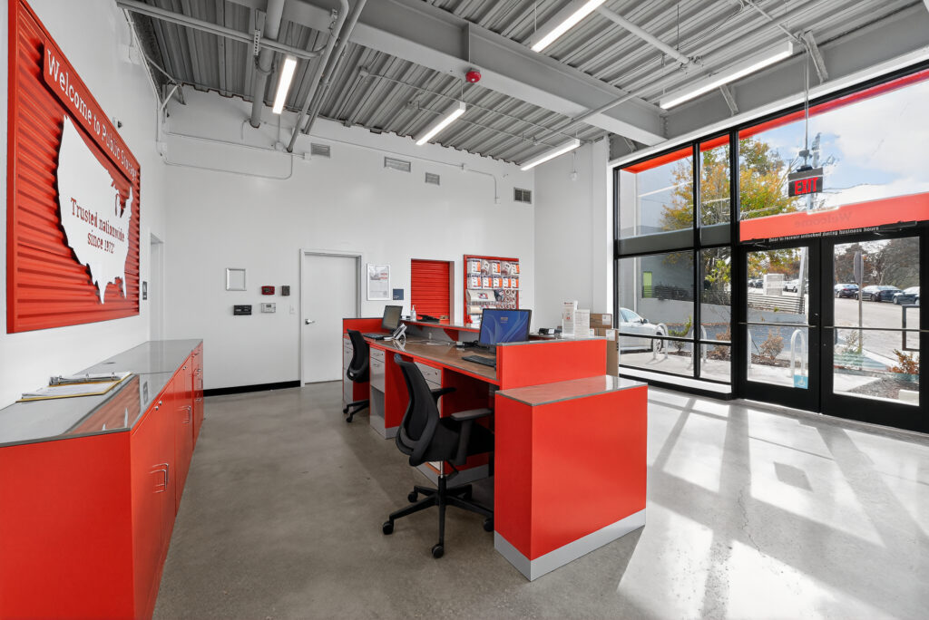 Interior of a self-storage office with red counters, two workstations, and a large sign on the wall featuring a map of the United States.