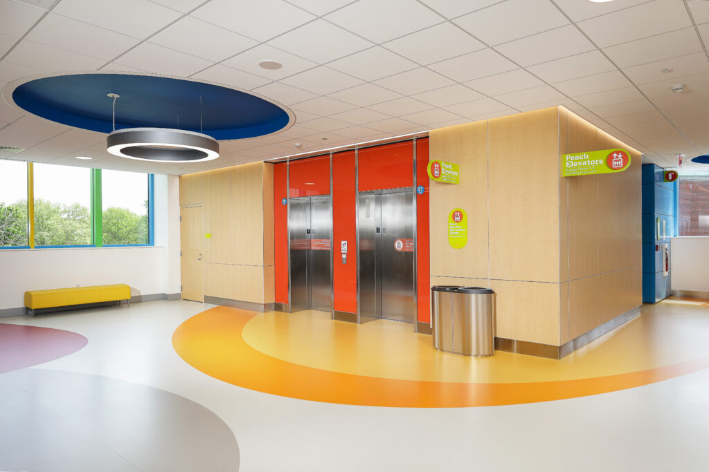 An elevator lobby with two stainless steel elevators, orange wall panels, and signs directing to the Peach Elevators.