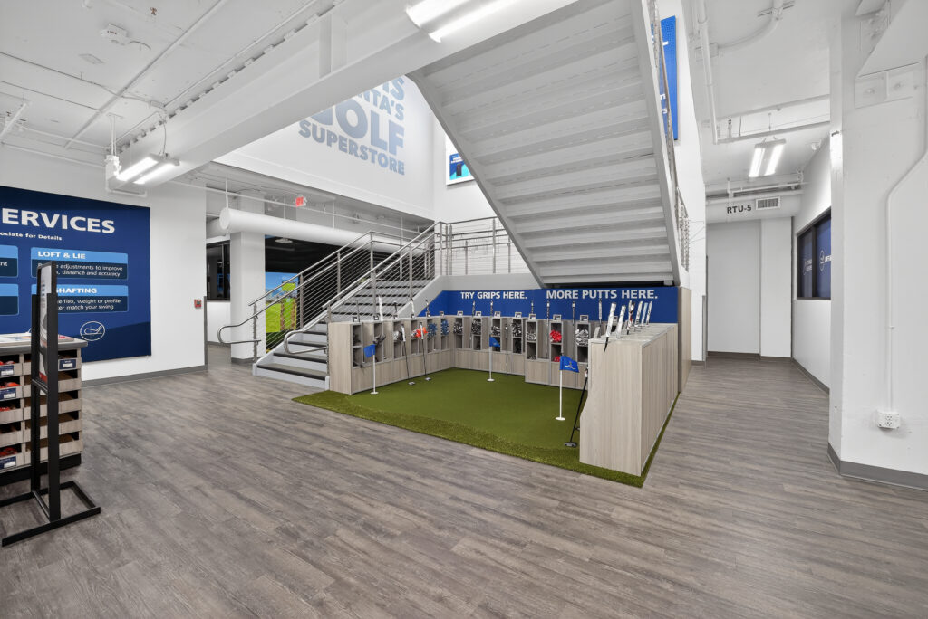 Interior of a golf store featuring a putting green display, club storage cubbies, and a central staircase.