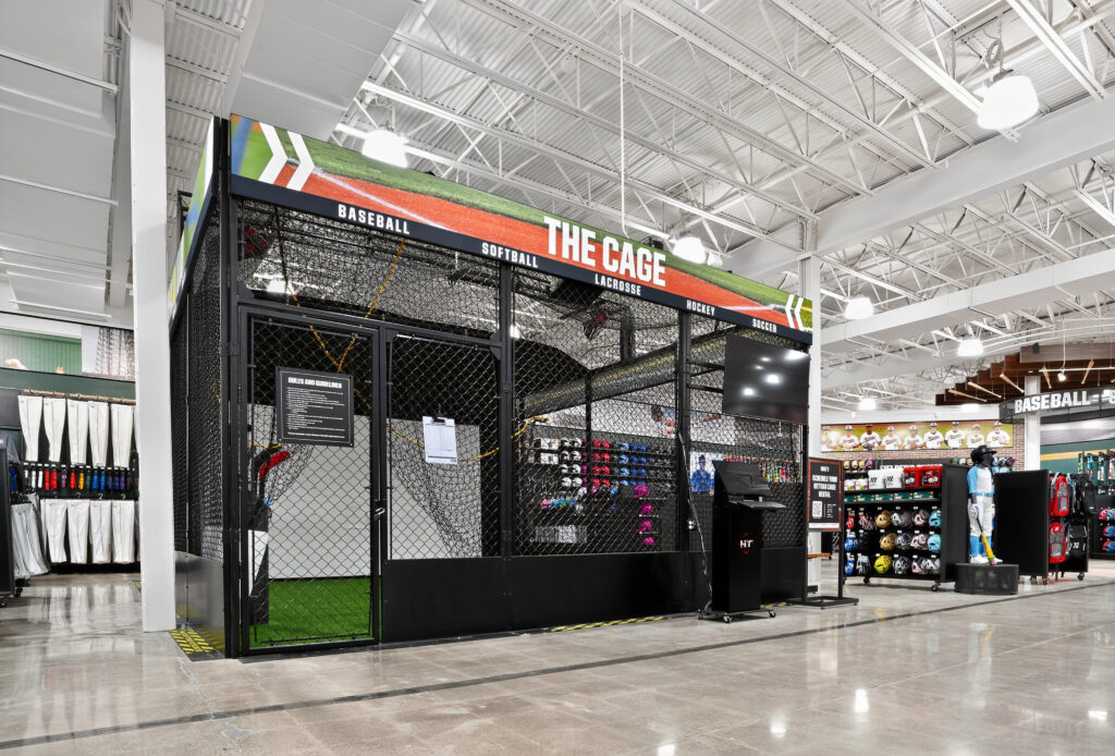 An indoor batting cage named “The Cage” in a sporting goods store, offering baseball, softball, lacrosse, hockey, and soccer training.