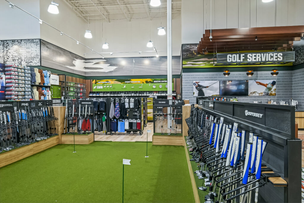 Interior of a golf retail store featuring aisles of golf clubs, accessories, and a putting green.