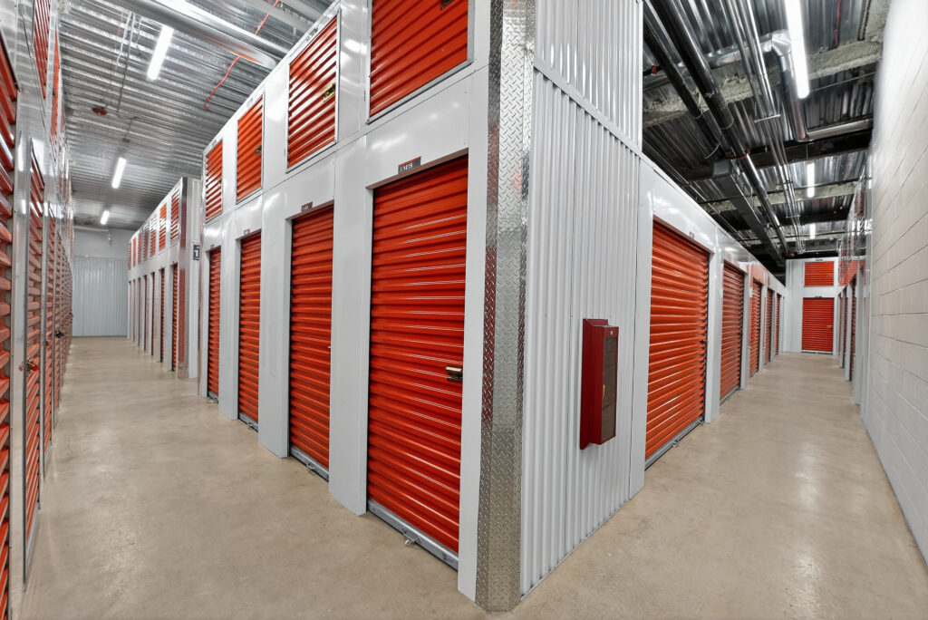 Rows of orange roll-up storage unit doors in a brightly lit indoor facility.