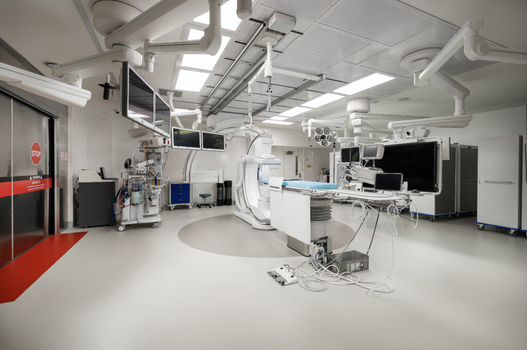 Modern surgical operating room with an imaging system, procedure table, and multiple medical monitors.