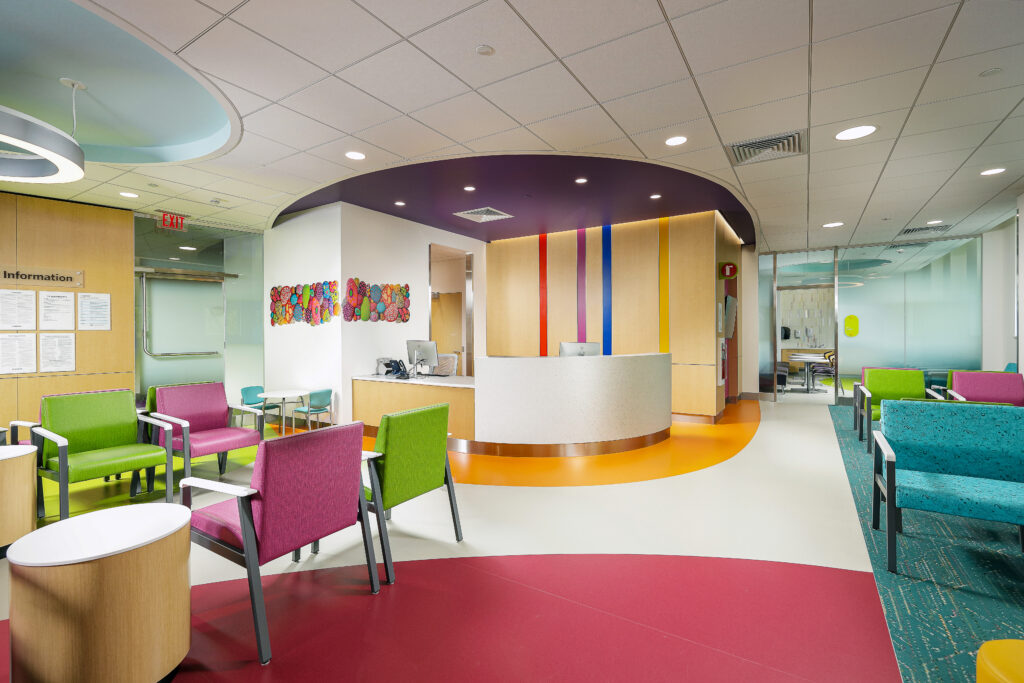 Reception area of a medical facility with a curved desk, colorful chairs, and circular floor patterns.