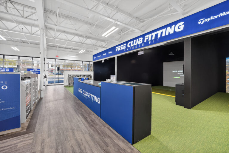 A golf club fitting station with a service counter, a golf simulator screen, and TaylorMade signage.