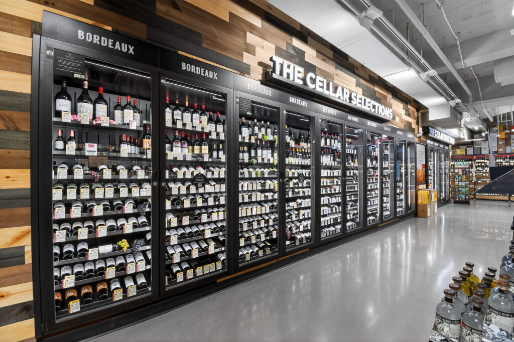 Wall of refrigerated glass wine cabinets labeled “The Cellar Selections” in a retail store, with shelves organized by region.