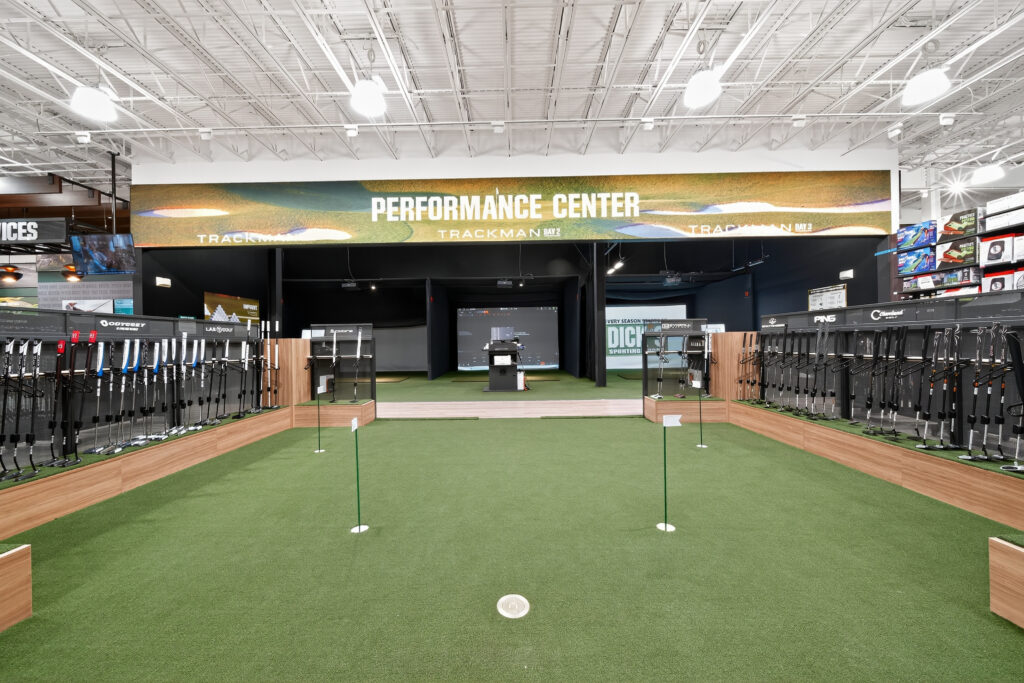 Indoor golf performance center with a putting green and rows of golf clubs on display.