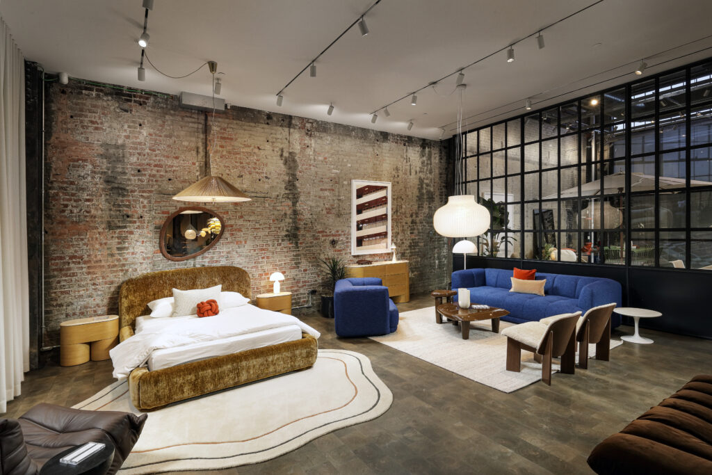 A studio space with a bed, a blue sofa, and modern furniture against an exposed brick wall.