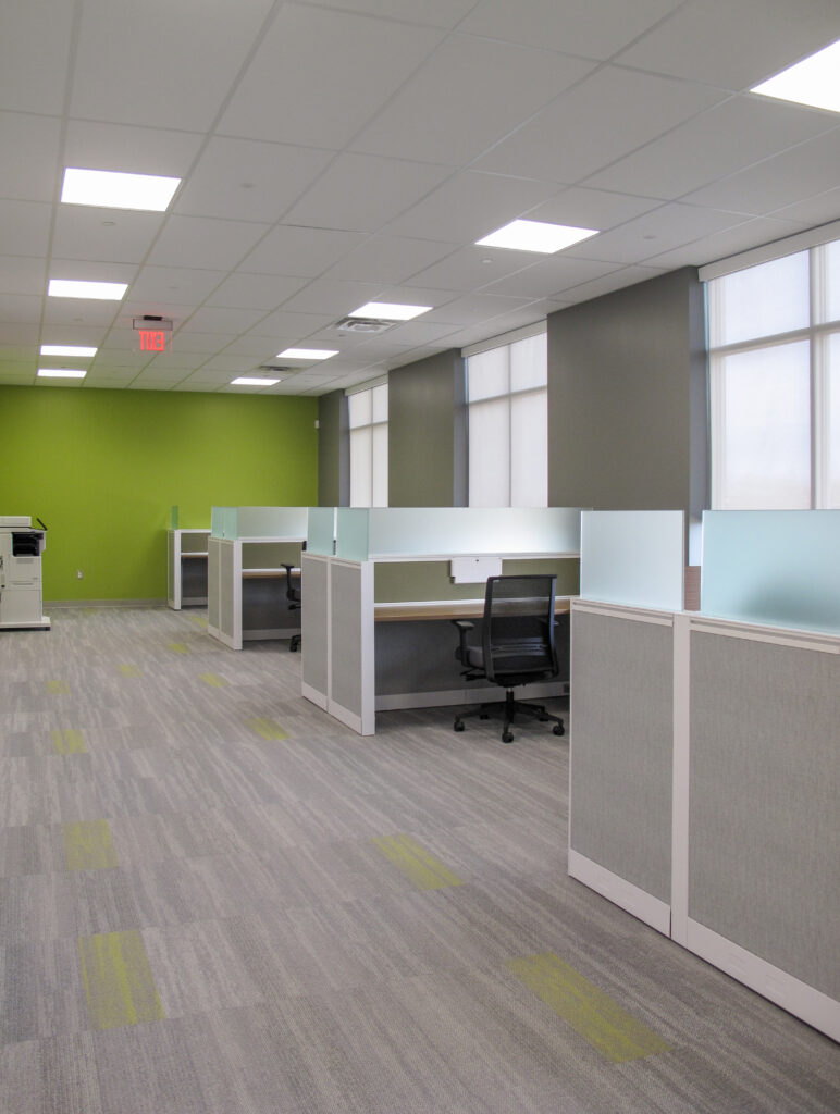 Empty office space with rows of cubicles, a lime green accent wall, and a printer in the corner.